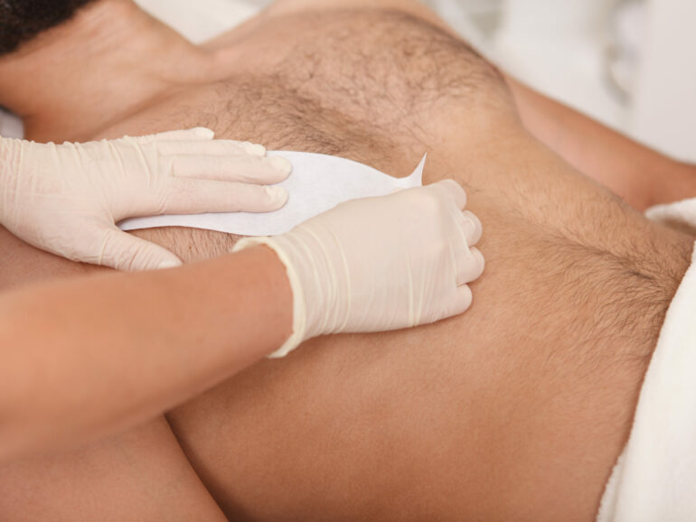 Cosmetologist doing waxing on torso of unrecognizable male client