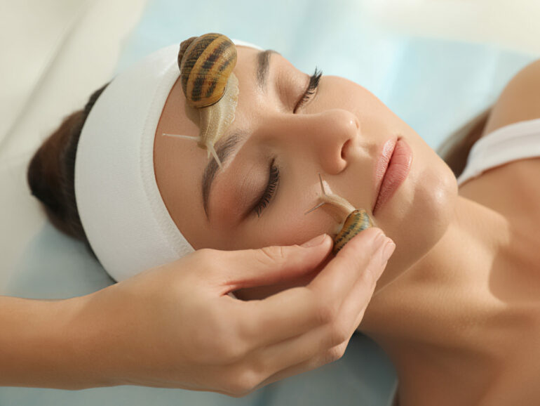 Young woman receiving snail facial massage in spa salon, closeup