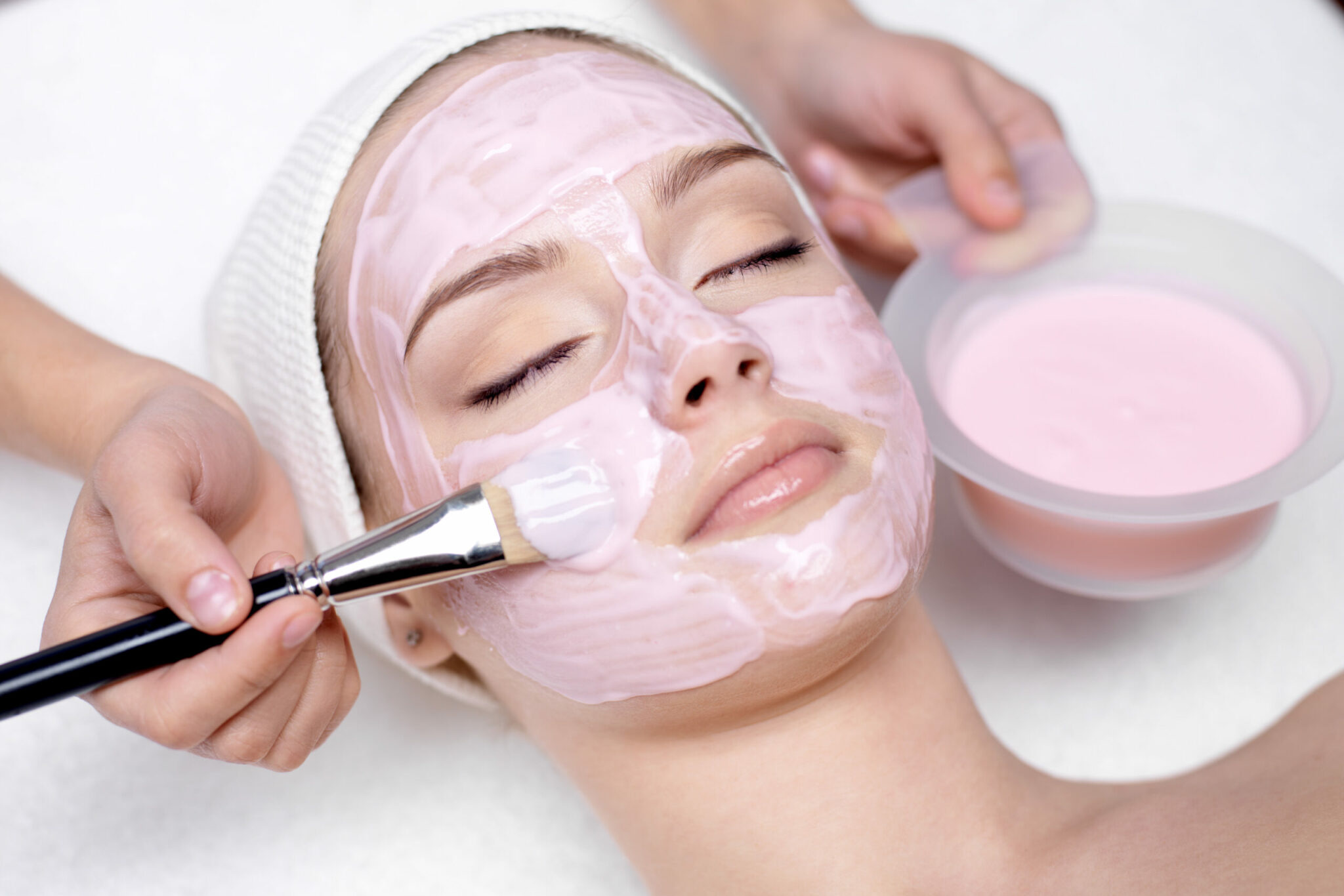 Young beautiful girl receiving pink facial mask in spa beauty salon - indoors