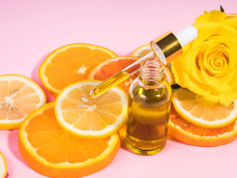 Vitamin C serum bottle with dropper on pink background with orange citrus slices. Natural anti aging skin care concept