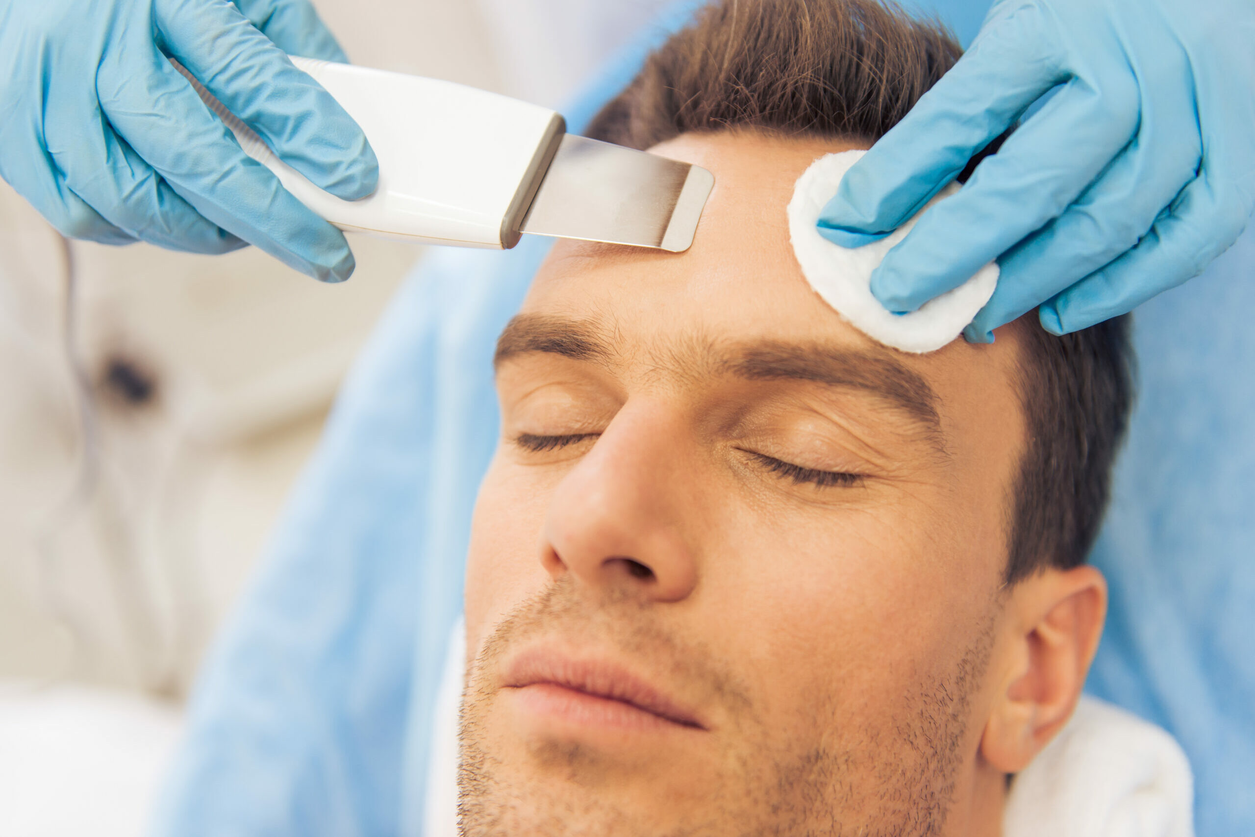 Portrait of handsome man getting face skin treatment, close-up. Doctor is undertaking the procedure using a modern equipment