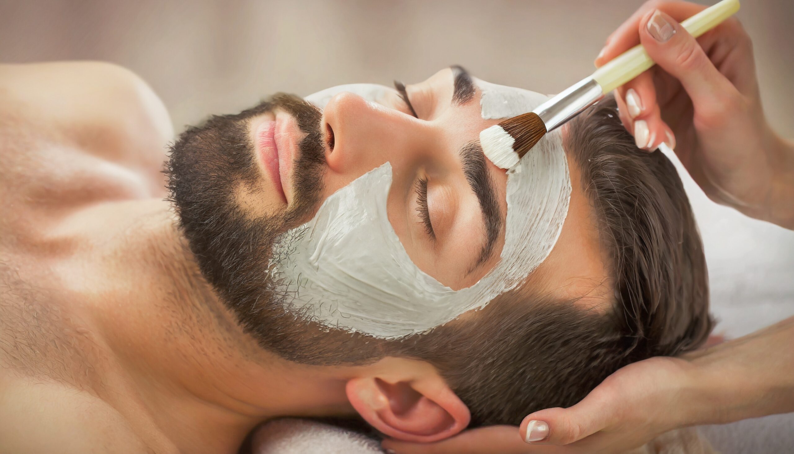 Man receiving a Facial Clay Mask in Wellness Resort or Spa - Relaxation and Skin Care done by Beautician